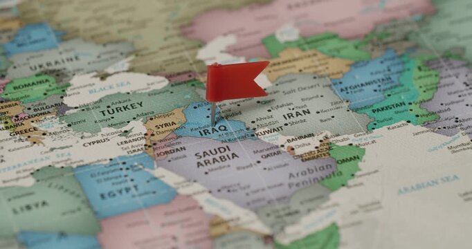 Macro shot showing a red flag pin placed on the country of Iraq on a political world map, indicating a specific travel destination, a point of interest, or a strategic location