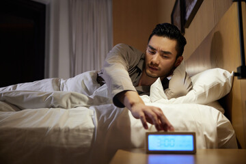 Obraz premium Tired man with insomnia reaching for alarm clock at night