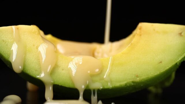 Pouring sweet condensed milk onto a halved avocado on a black background.