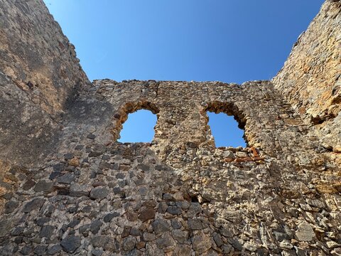 Scenic view of the historic Red Tower (Kızılkule) from inside the ancient fortress walls in Alanya, Turkey, featuring a blue sky, stone walkway, and coastal harbor background.