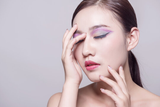 Beauty portrait of young woman with colorful eye makeup touching her face