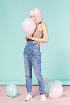 Playful young woman with pink hair and balloons in a studio