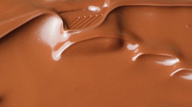 Melted milk chocolate wave submerging single chocolate square close up