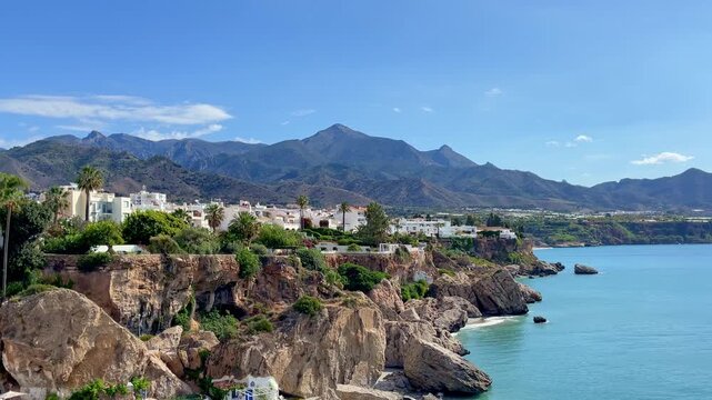 scenic view of coastal town with white houses on rocky cliffs facing sea and mountains under clear blue sky- Nerja, province of Malaga in Spain