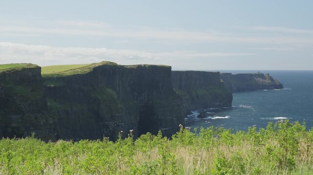 Wide view along the Cliffs of Moher, with sheer rock walls, green cliff tops and the Atlantic Ocean extending along the coast of County Clare, Ireland.