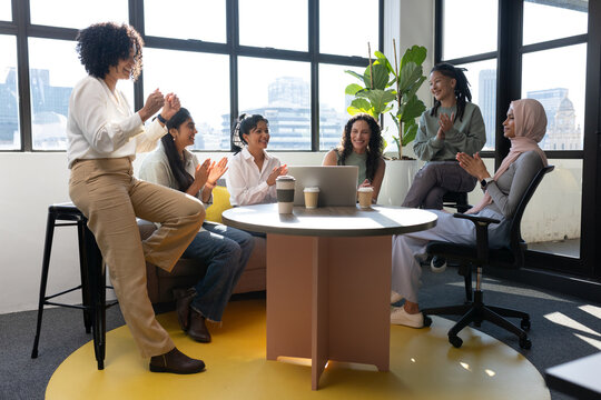 Diverse coworkers applauding and celebrating in office lounge around laptop and takeaway cups