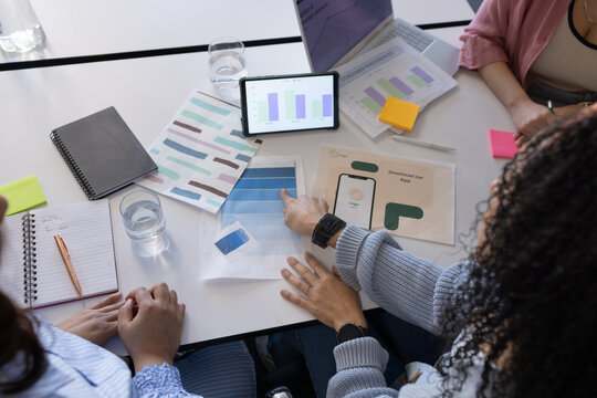 Three African American women examining tablet bar chart, pointing blue swatch in office