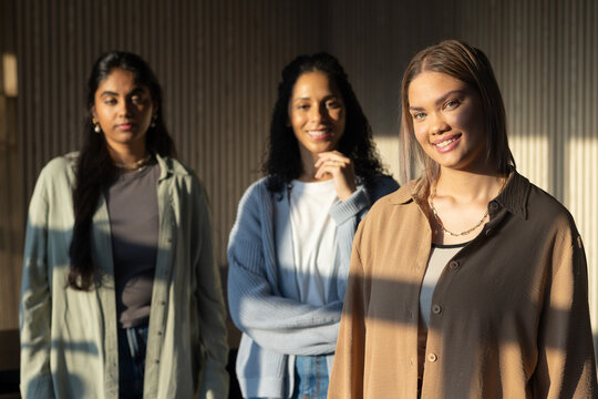 Diverse female friends posing in soft studio on vertical slat wall with sunlight bands, copy space