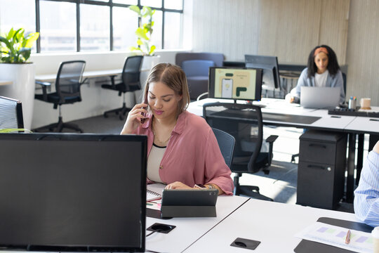 African American woman wearing pink blouse using smartphone and tablet, checking notebook at office