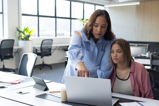 African American women working at desk, wearing striped blouse and pink jacket pointing at laptop