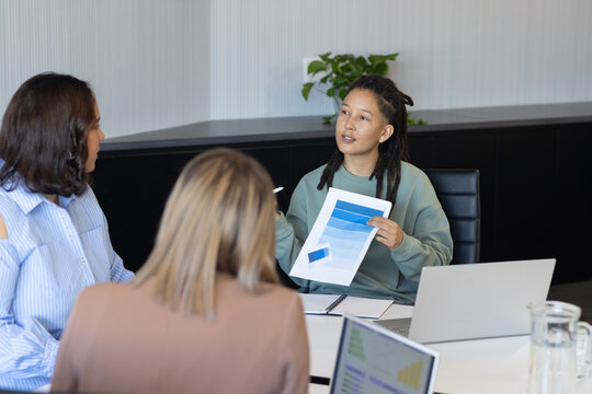 African colleagues sitting at white table in office, presenter in green top holding blue bar chart