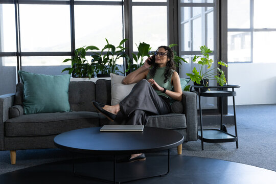 African American woman in green top, sitting in office, holding phone, closed laptop, copy space