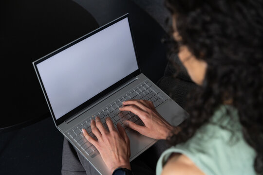 African American woman typing on laptop in lap at home, green top, smartwatch, coffee table left