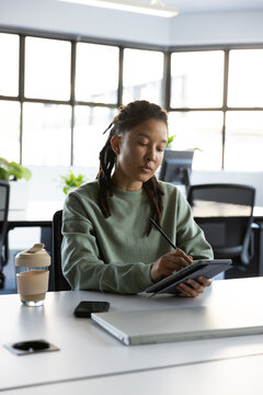 Non-binary African American sitting at desk drawing on tablet with stylus in office near laptop