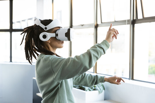 Non-binary person wearing white VR headset and green sweatshirt at studio windows using VR controls