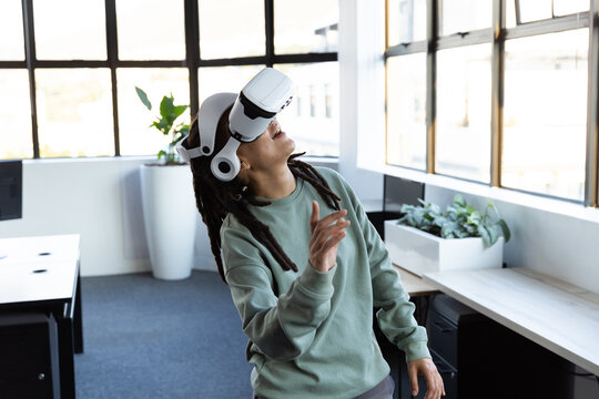 African American nonbinary standing in office wearing green crewneck white VR gear reaching planter