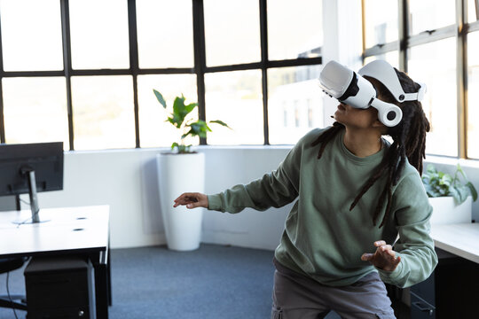 African nonbinary adult standing right of office wearing sage top white VR headset reaching screen