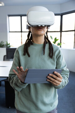 Non-binary adult standing in office wearing green sweatshirt and white VR headset holding tablet