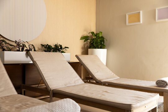 Three beige cushioned wooden chaise lounges are occupying frame in spa lounge with rolled towel