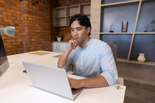 Adult man sitting at desk in office, wearing light blue shirt, using laptop with green lamp