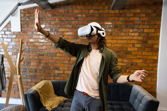 African American man wearing white VR headset and reaching out in loft lounge with mustard throw