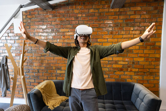 African American man wearing white VR headset standing in living room lounge reaching toward sofa