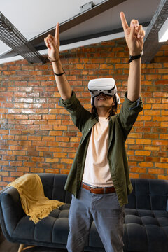African American man standing in loft by brick wall, wearing VR headset, pointing upward