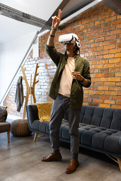 African man standing in loft lounge interacting with VR headset near blue sofa and brick wall