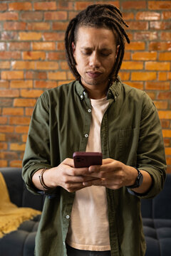 Man standing and checking red-cased smartphone in living room with brick wall, wearing olive shirt