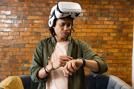 African American man standing in lounge adjusting black smartwatch while wearing white VR headset