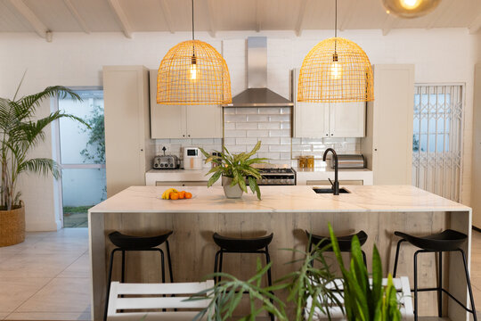 Kitchen island is featuring marble counter in coastal kitchen with rattan pendants, black stools