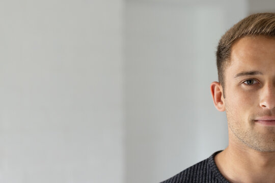 Man posing at right against off-white wall wearing dark sweater, looking toward camera, copy space
