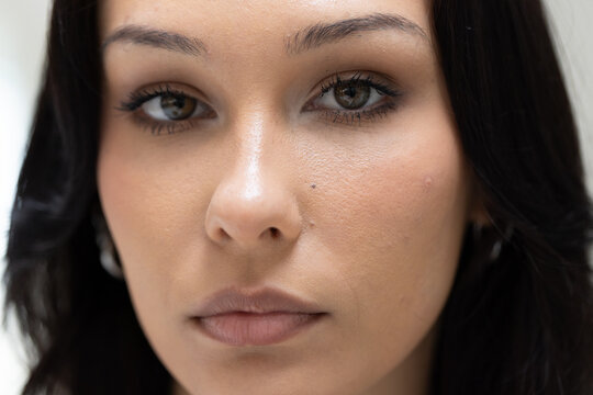 Woman in her twenties posing in studio, showing silver hoop earring, neutral lipstick, mole