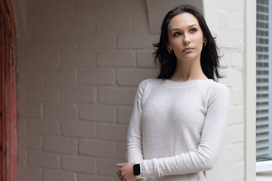 Female leaning against painted brick wall in alcove, wearing knit sweater and smartwatch