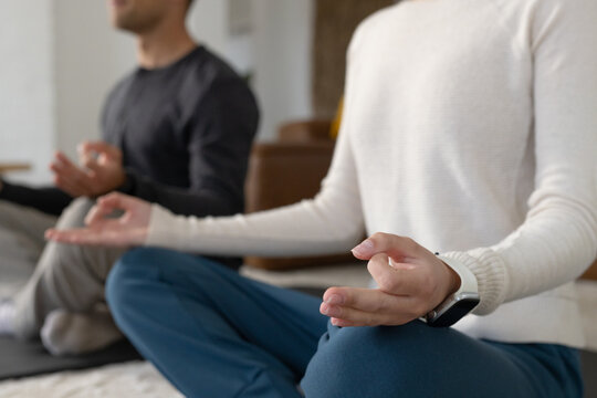 Couple meditating cross-legged on yoga mats in living room, wearing white sweater and smartwatch