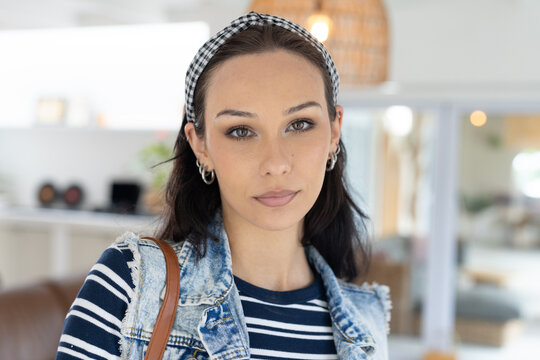 Woman standing facing camera in modern living area wearing denim vest striped top gingham headband