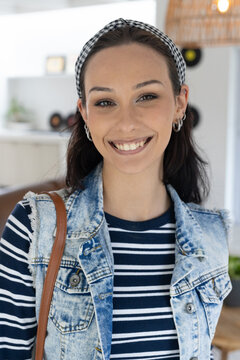 Adult woman standing and smiling at home, wearing checkered headband, denim vest