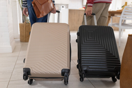 Couple standing in kitchen packing beige and black suitcases with spinner wheels