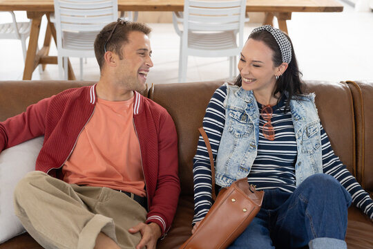 Couple sitting on brown leather sofa in bright living area, laughing with tan bag and sunglasses