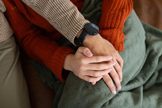 Diverse couple sitting on couch holding hands over green throw showing sweater and black smartwatch