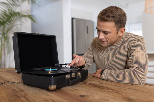 Adult man leaning guiding tonearm toward spinning blue-label vinyl on suitcase turntable in kitchen