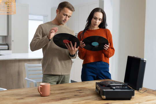 Couple checking vinyl records at table in kitchen, woman in orange sweater by open turntable