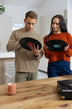 Couple wearing knits holding vinyl records and inspecting labels at kitchen table with turntable