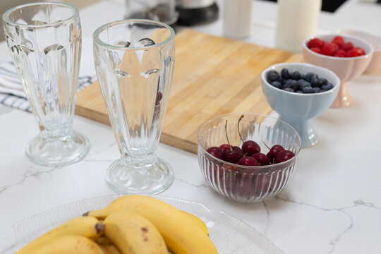 Two tall clear sundae glasses standing on marble counter with bananas, cherries