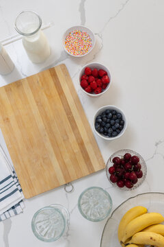 Bamboo cutting board sitting left on marble, soft light showing milk bottle, bowls, cherries