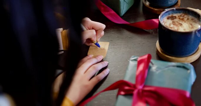 Hands are steadying gift tag on dark table writing label with blue pen for gift giving