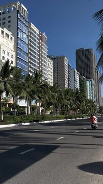 Urban street lined with tall buildings and palm trees under a clear blue sky. The scene captures a vibrant city atmosphere.