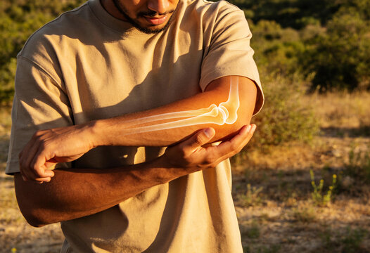 Man holding pained elbow joint with glowing anatomical bone illustration outdoors in golden sunset light medical health wellness concept