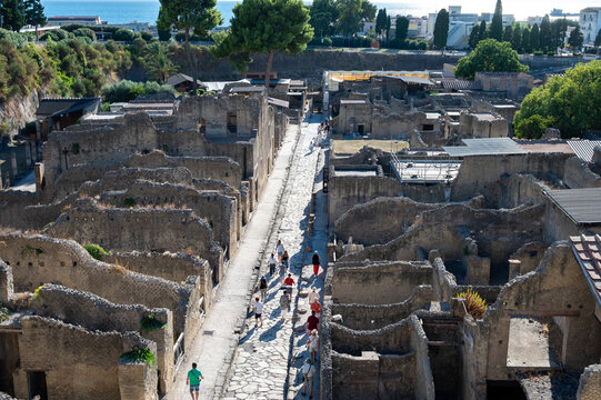 High-angle view of tourists walking along ancient stone streets past historic ruins in the archaeological site of Herculaneum, Italy