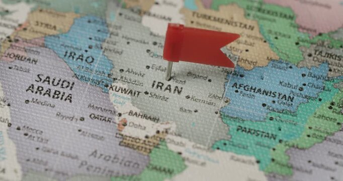 Human hand placing a red flag pin on the country of Iran on a political world map, indicating a travel destination, a point of interest, or a geopolitical situation in the Middle East region